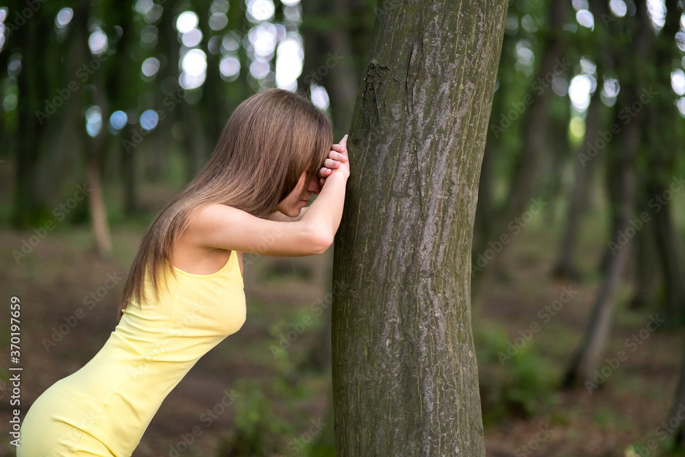 Young woman leaning to tree trunk in summer forest.