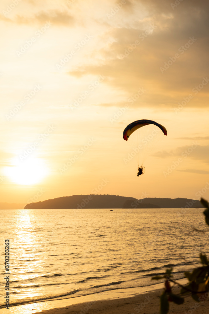 A paraglider swooping low over a Thai beach as the sun begins to set in the background