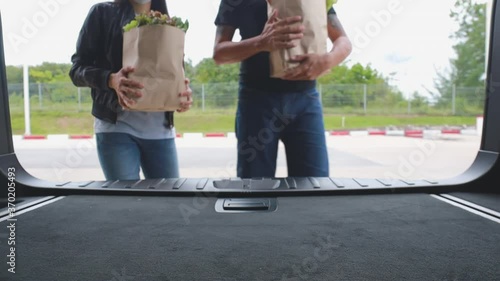 HD man and women a couple walk together on parking lot with shopping cart and shopping bag  full with fruit and vegetable and drop paper bag inside car. Shot from inside car. Family lifestyle concept