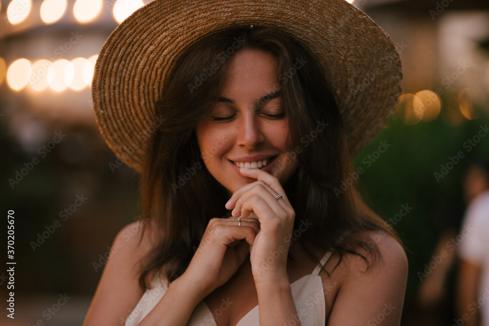 Young beautiful woman wearing straw hat and linen beige suit posing on a city street in old town at sunset.