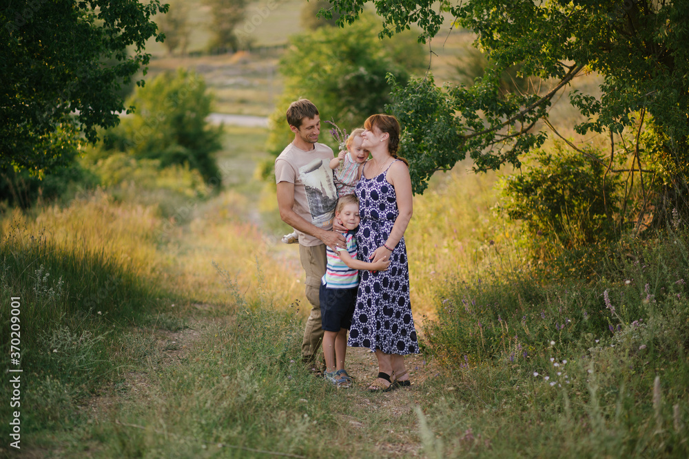 Happy family of young parents and their little children walking in a forest at sunset. Happy family of young parents and their little children walking in a forest at sunset.