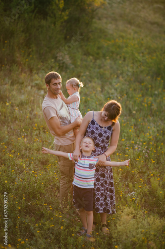 Happy family of young parents and their little children walking in a forest at sunset.