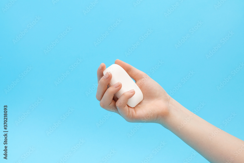 A soap bar in a woman's hand, blue background.