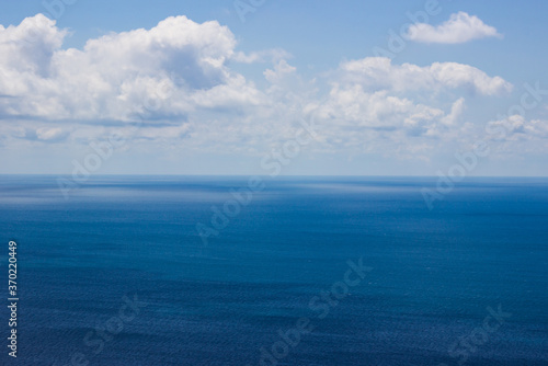 Photo of a bright blue sea to the very horizon and cumulus clouds in the blue sky