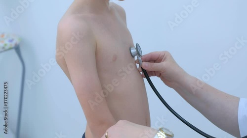 Doctor pediatrician cardiologist listening heartbeat exam of patient child boy using stethoscope on pediatric checkup appointment, children medical healthcare concept. Counting heart beats in minute. photo