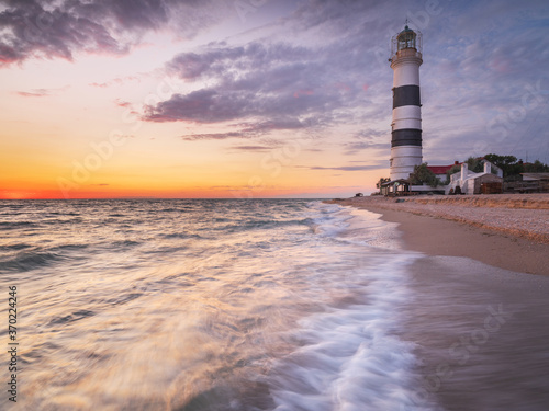 evening scene of beach with sea smooth water and lighthouse with copy space in the sky