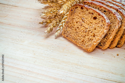 Whole wheat bread. Fresh loaf of rustic traditional bread with wheat grain ear or spike plant on wooden texture background. Rye bakery with crusty loaves and crumbs. Homemade baking.