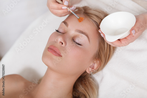Close up of a cosmetologist applying peeling liquid on the face of female client photo
