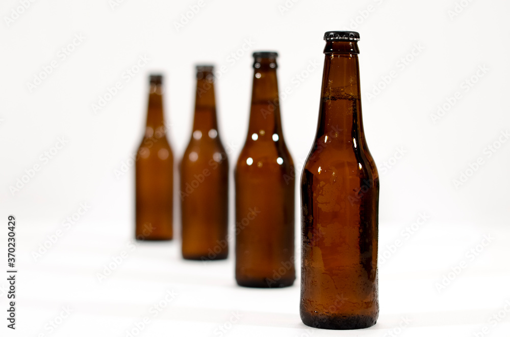 Four brown glass bottles of beer in line moving away from the first one on a white background. Four brown glass bottles of beer in line moving away from the first one on a white background.