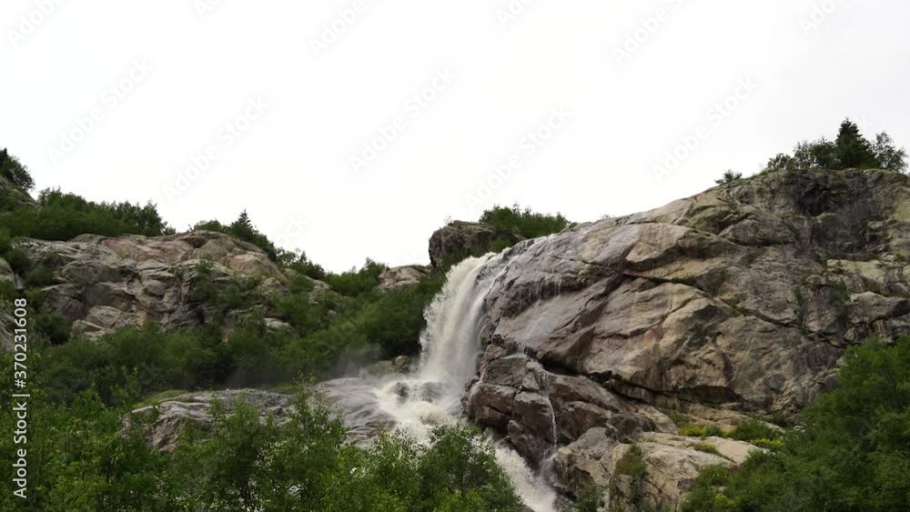 Waterfall on summer day in nature. Rapid water stream falling from rocks against blue sky on sunny summer day in countryside Waterfall on summer day in nature. Rapid water stream falling from rocks against blue sky on sunny summer day in countryside