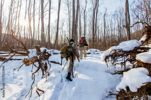 January, 2016 - Agzu, Primorsky Territory - Udege hunters with guns walk through deep snow in the taiga. Wild animal hunting in Russia