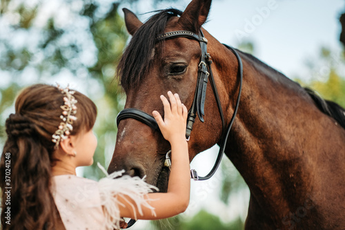 A little girl strokes a horse her favorite horse on the head. Communication of a child with a horse in the summer.