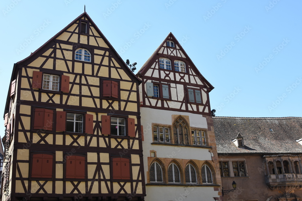 Facades of two gable roof half-timbered houses built in traditional architecture of Alsace in Colmar, France. The facades are embellished with dark colored wooden balks or beams.