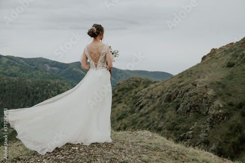 Beautiful bride on a background of autumn mountains with her back. The wind blows her hair. Wedding ceremony at the top of the mountain. Free place.