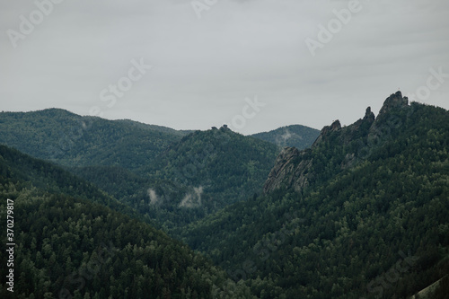 Gloomy view to great mountains under dark gray cloudy sky. Dramatic landscape with mountains in rainy weather. Atmospheric scenery with giant mountain ridge in overcast darkness.