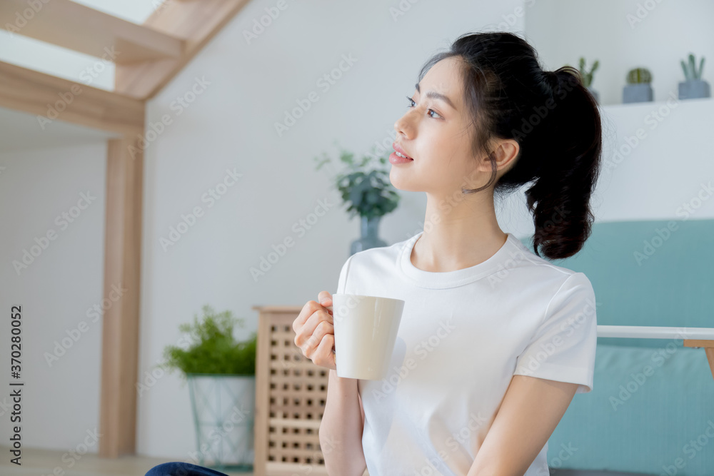 Young asia woman with ponytail in white t-shirt holding a cup of coffee or tea relaxing at home in the morning. Young asia woman with ponytail in white t-shirt holding a cup of coffee or tea relaxing at home in the morning.