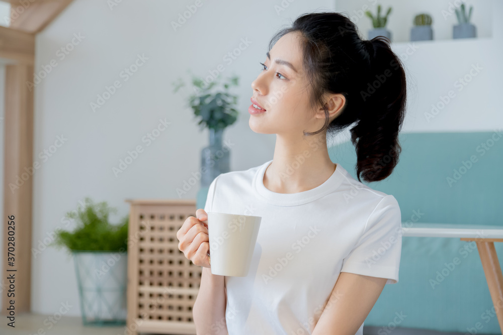 Young asia woman with ponytail in white t-shirt holding a cup of coffee or tea relaxing at home in the morning. Young asia woman with ponytail in white t-shirt holding a cup of coffee or tea relaxing at home in the morning.