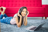 Beautiful young asian woman listening to music online with headphones while lying on carpet