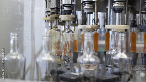 Spill of brendy in glass bottles at distillery. Glass bottle filling machine in factory. Spillage of alcoholic beverages. Production process of alcoholic beverages in modern factory.