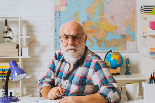 A teacher who works professionally. A teacher who knows a lot. Portrait of senior teacher sitting at desk in classroom. photo