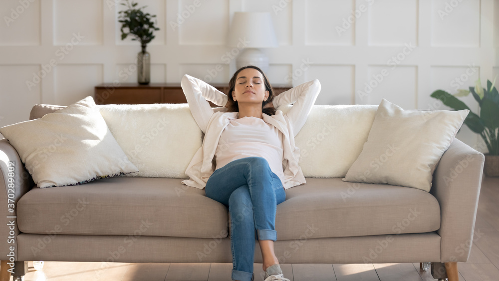 Front view relaxed young 30s woman sleeping on comfortable couch with folded hands behind head, enjoying weekend leisure lazy time, napping daydreaming or meditating alone in modern living room. Front view relaxed young 30s woman sleeping on comfortable couch with folded hands behind head, enjoying weekend leisure lazy time, napping daydreaming or meditating alone in modern living room.