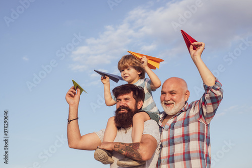 Young boy with father and grandfather enjoying together in park on blue sky background.
