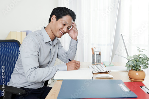 Smiling young businessman writing down his ideas and plans for the day