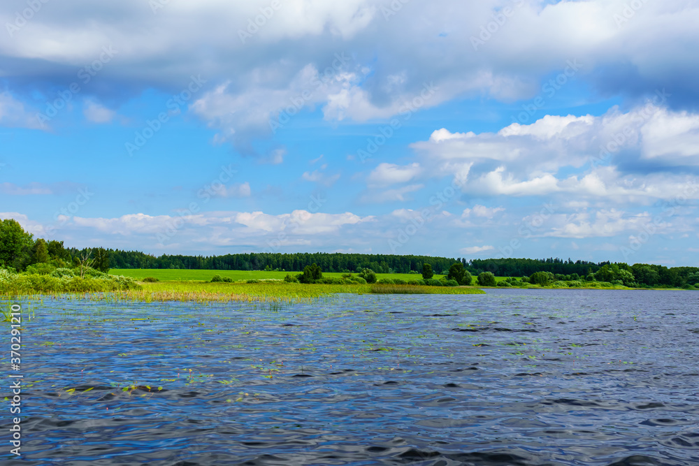 Waves in the lake reflect blue sky and green meadow in the background Waves in the lake reflect blue sky and green meadow in the background