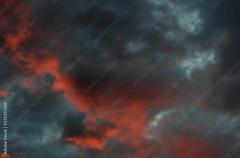 Dramatic blue-black sky with orange clouds and gaps between them during sunset