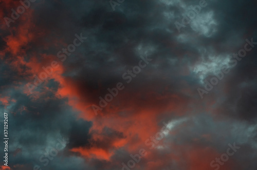 Dramatic blue-black sky with orange clouds and gaps between them during sunset