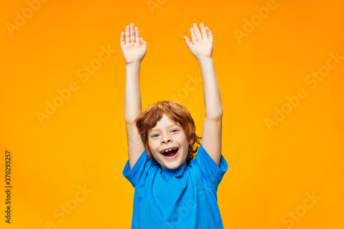 Red-haired boy with his hands up on a yellow background 