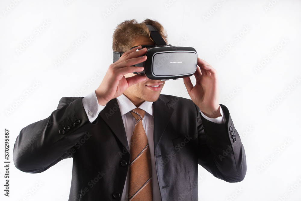 A male businessman in a black suit and tie wearing a virtual reality helmet see images, on a white background