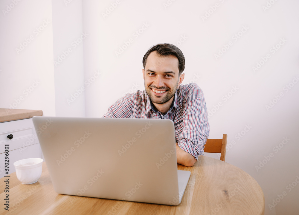 Happy smiling man in shirt with a cup of coffee works on laptop Happy smiling man in shirt with a cup of coffee works on laptop