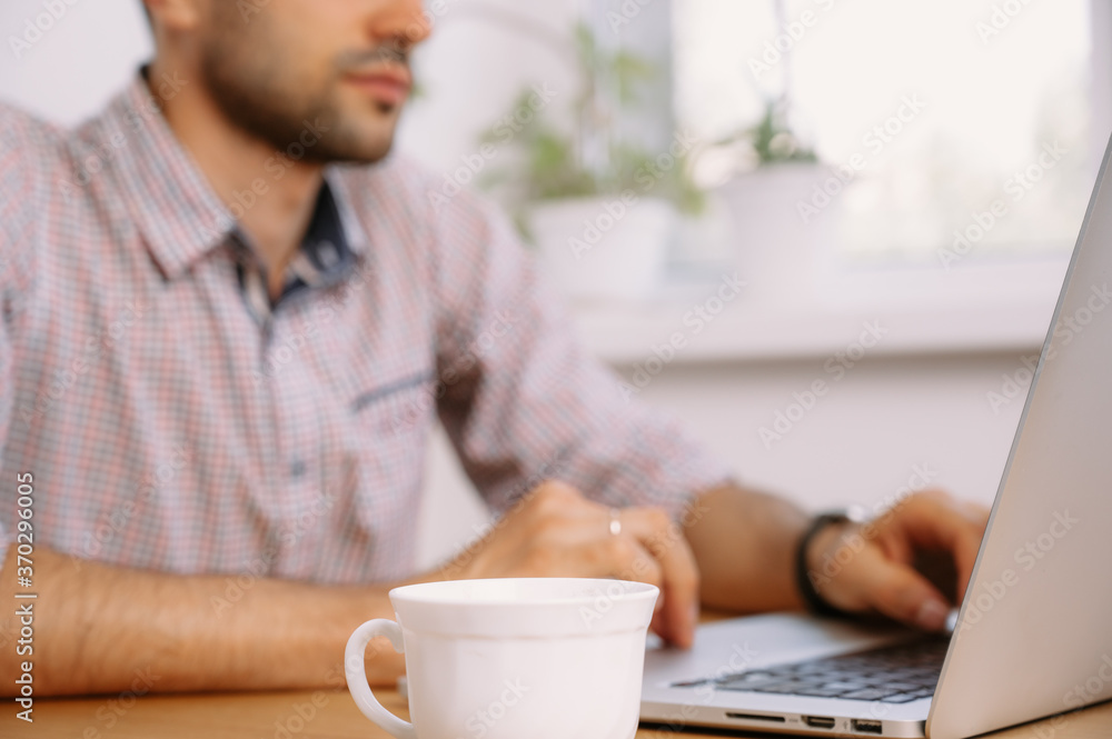 man in shirt with a cup of coffee works on laptop man in shirt with a cup of coffee works on laptop