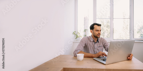 man in shirt with a cup of coffee works on laptop © Alexander