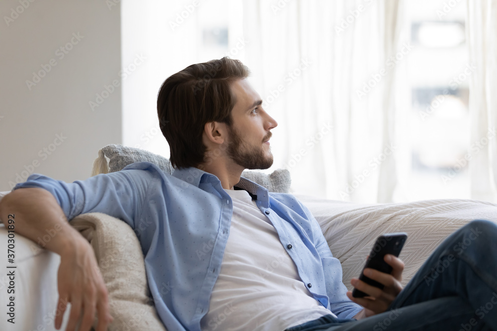 Dreamy thoughtful young man relaxing, holding smartphone, enjoying leisure time at home, peaceful satisfied guy looking in distance, dreaming, visualizing, chatting online, surfing internet Dreamy thoughtful young man relaxing, holding smartphone, enjoying leisure time at home, peaceful satisfied guy looking in distance, dreaming, visualizing, chatting online, surfing internet