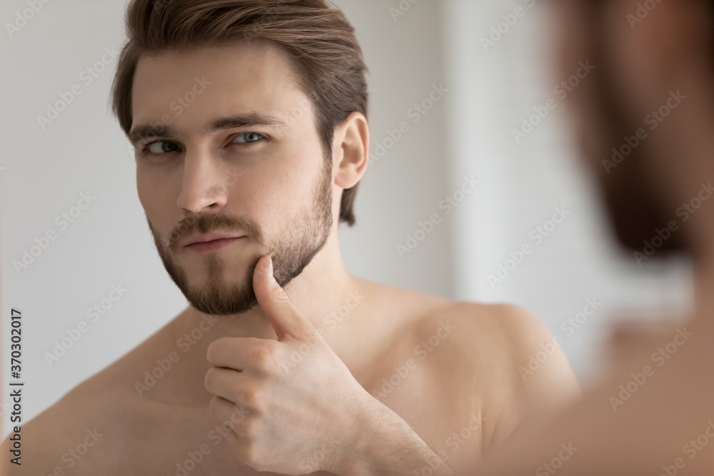 Close up headshot mirror reflection satisfied handsome young man touching beard, standing in bathroom, applying aftershave lotion, enjoying skincare procedure, morning routine concept Close up headshot mirror reflection satisfied handsome young man touching beard, standing in bathroom, applying aftershave lotion, enjoying skincare procedure, morning routine concept