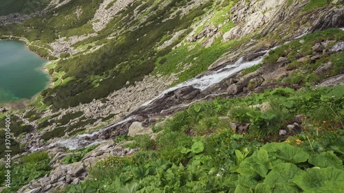 Scenic view of Velicky vodopad (Velicky waterfall) running down towards blue water of Velicke Pleso (Velicke tarn) in Slovakia, High Tatras mountains. Wild flowing water on rocky mountains photo