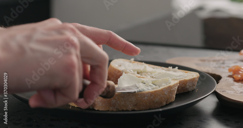 man spread cream cheese on ciabatta slice on black plate