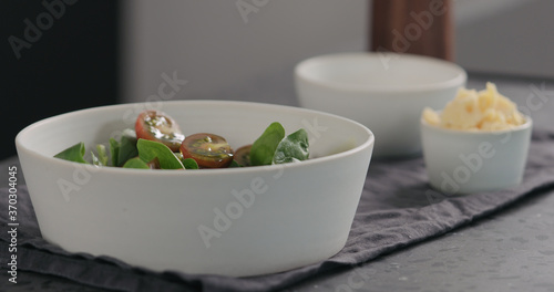 pour olive oil into salad with kumato tomatoes and spinach in white bowl