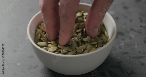 closeup of man hand takes pumpkin seeds from white bowl