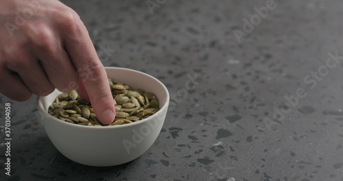 man hand takes pumpkin seeds from white bowl with copy space