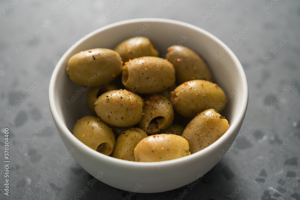 Closeup pitted whole green olives with spices in white bowl on terrazzo surface Closeup pitted whole green olives with spices in white bowl on terrazzo surface