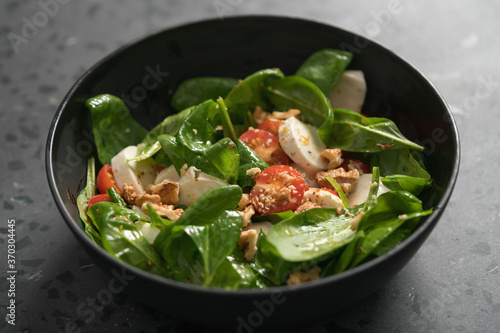Salad with spinach, tomatoes and mozzarella in black bowl on concrete countertop