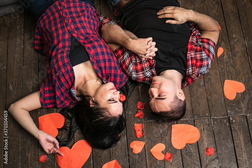 Top view of lovely valentine's couple looking at one another with red heart in their hands over the wooden background and paper hearts. Passionate male andfemale on the floor. Day of love photo