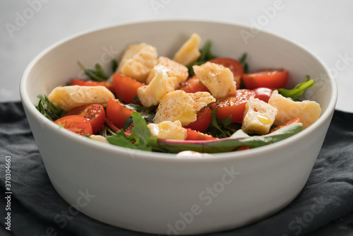salad with cherry tomatoes, mixed grens and cheese in white bowl on concrete background