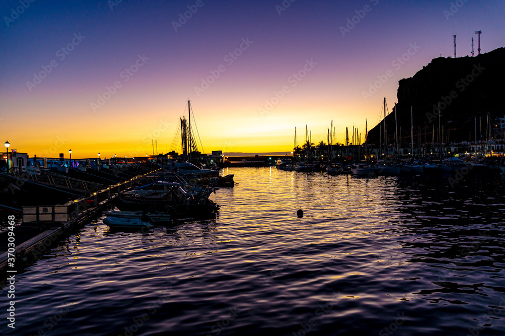 Puerto de mogán with its boats and sailboats with reflections of the night lights on the water