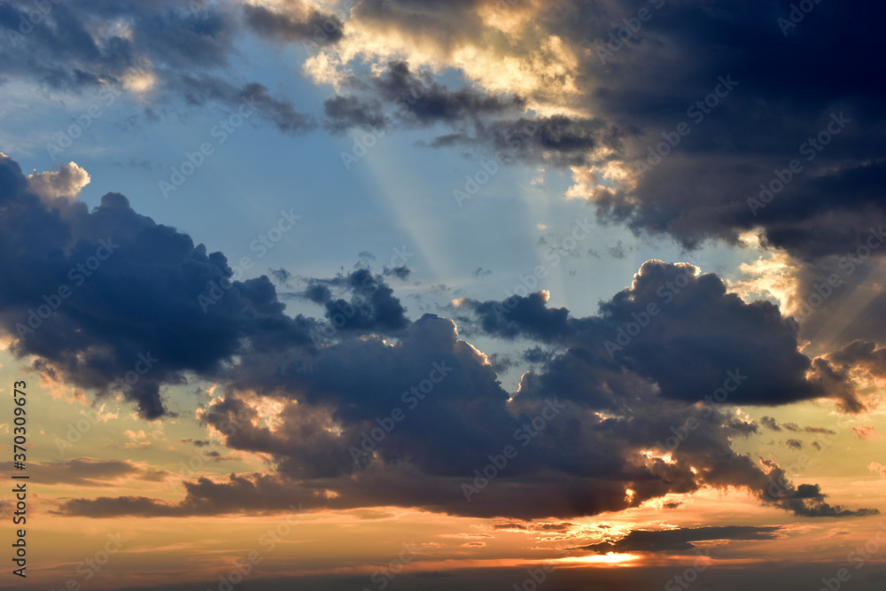 Evening sunset sky with yellow blue clouds and sun rays