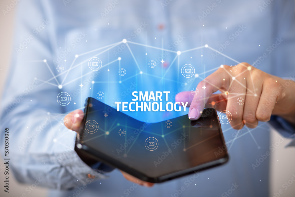 Businessman holding a foldable smartphone with SMART TECHNOLOGY inscription, new technology concept Businessman holding a foldable smartphone with SMART TECHNOLOGY inscription, new technology concept