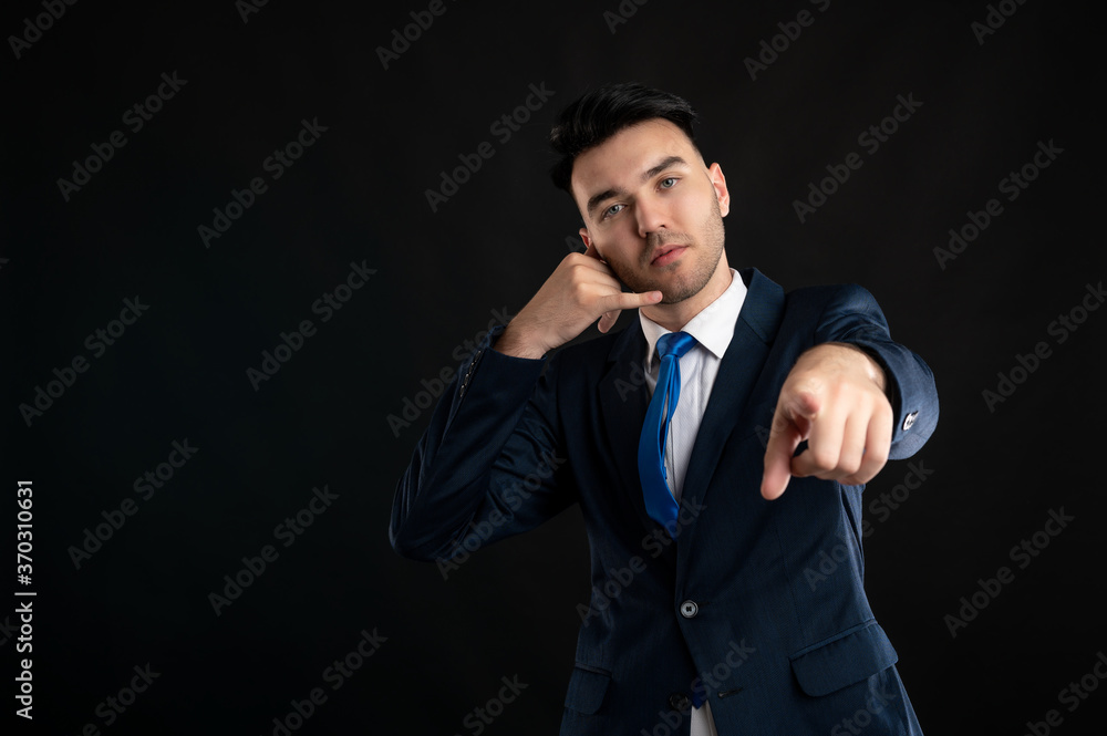 Portrait of business man wearing blue business suit and tie showing calling or contact gesture pointing at the camera Portrait of business man wearing blue business suit and tie showing calling or contact gesture pointing at the camera